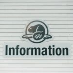 Close-up van een informatiebord op een gestructureerde witte muur, met een beversymbool